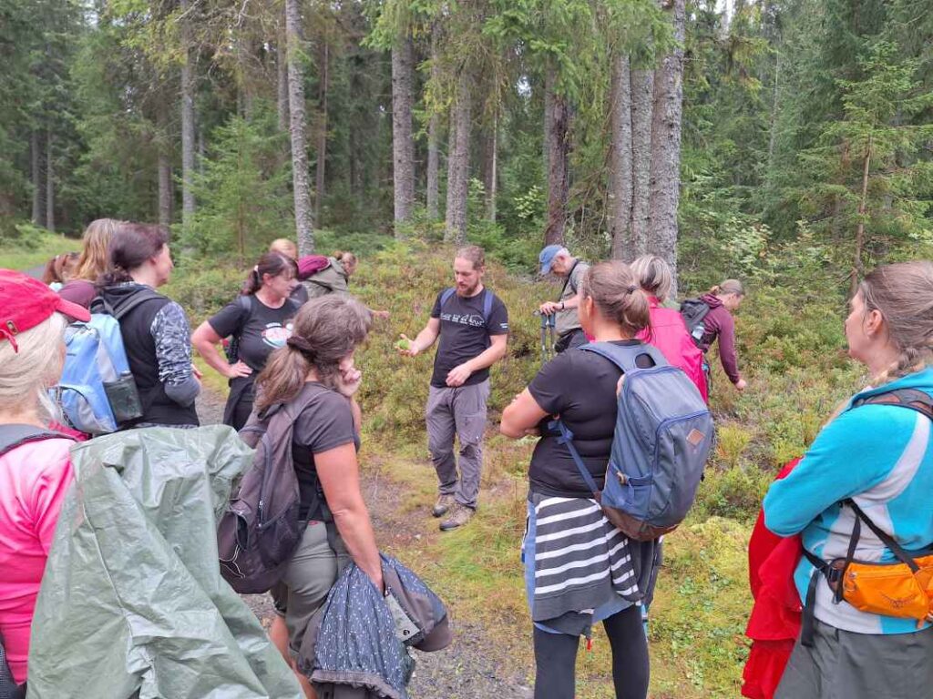 foto ze seminare Pojdme na to od lesa, účastníci naslouchají výkladu lektora, jsou na kraji lesa, v pozadí jsou stromy