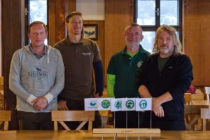 Fotografie zachycuje ředitele třech národních parků Krkonoše, Šumava a České Švýcarsko a koordinátora Acociace národních parků. Na stole je dřevěný stojan s pěti malými vlaječkami, které mají loga všech čtyřech českých národních parků a Asociace NP. Muži jsou oblečeni v neformálním oblečení. Prostředí působí komunitně a přátelsky, jedná se o setkání zástupců národních parků.