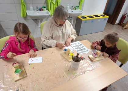 Bezbariérová Lesní dílna Stožec, pohled do učebny, kde právě dvě holčičky s lektorkou malují stopy.