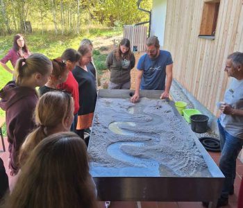 seminar Kralovstvi vod a mokřadů, účastníci stojí u modelu krajiny a lektor jim ukazuje, jak meandruje řeka